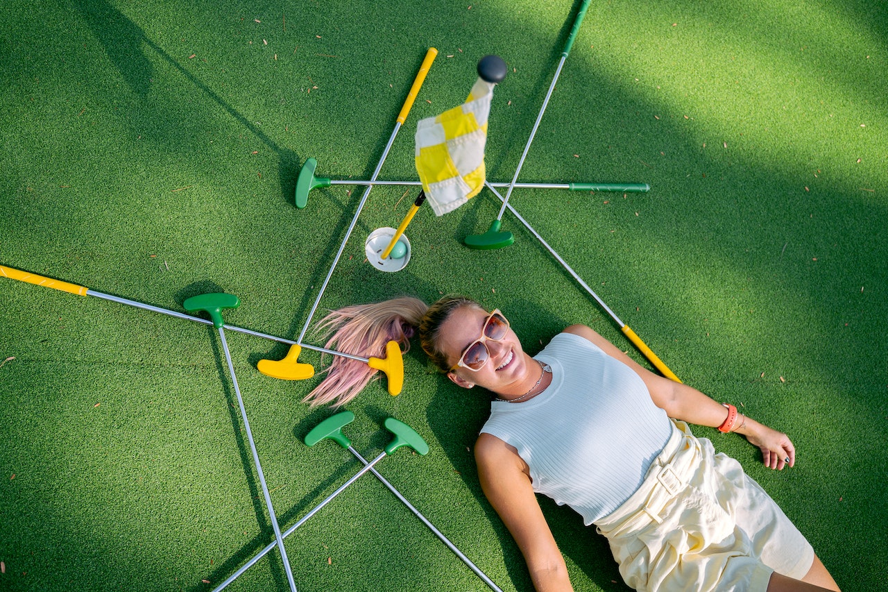 jeune femme allongée sur un green de golf entouré de putter de golf
